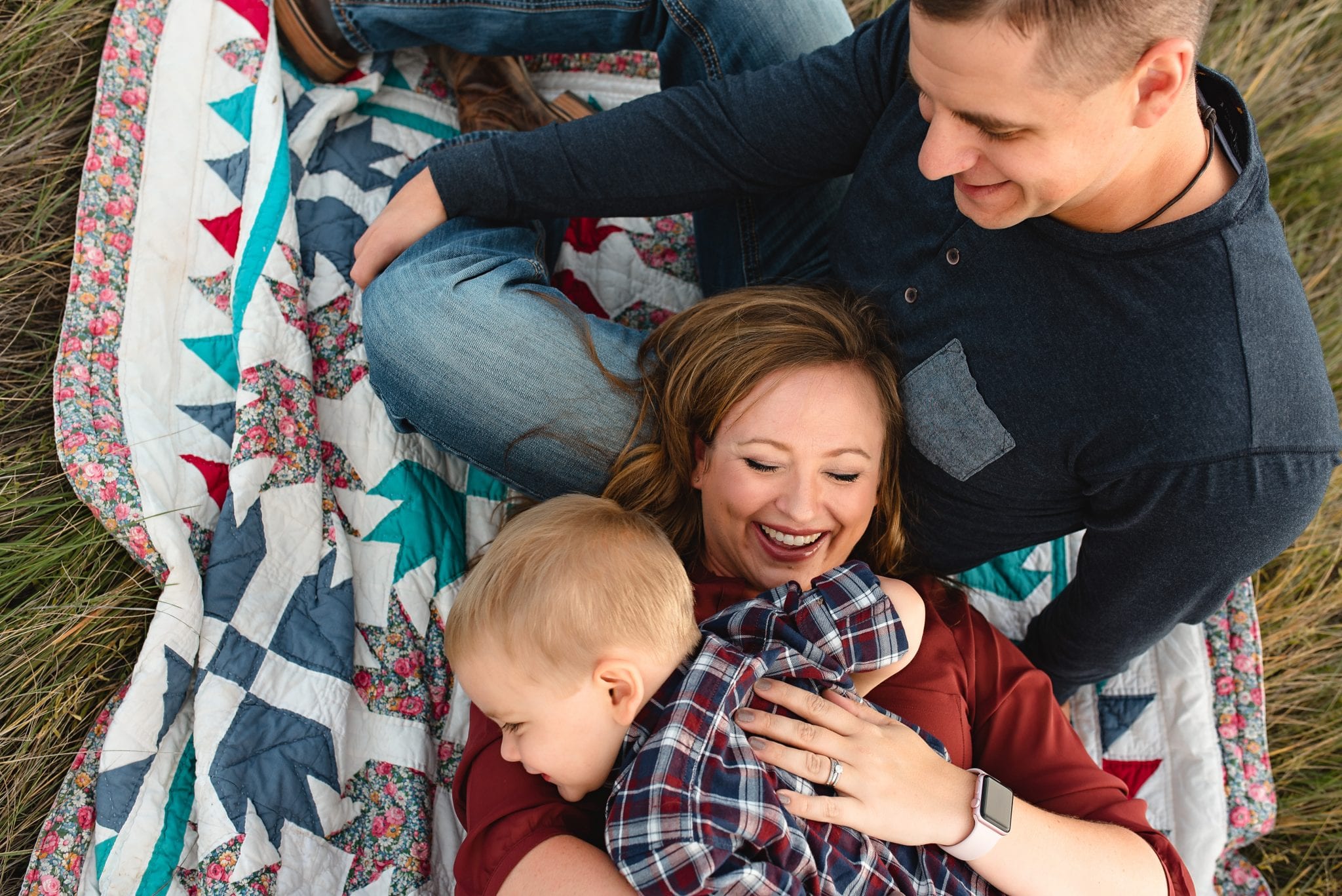 family of 3 snuggling in a field laughing