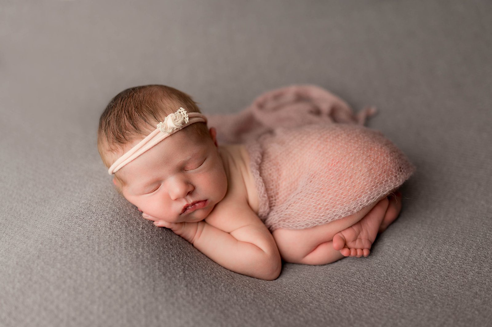 newborn baby tushy up pose with gauzy cover and pink floral headband on gray backdrop